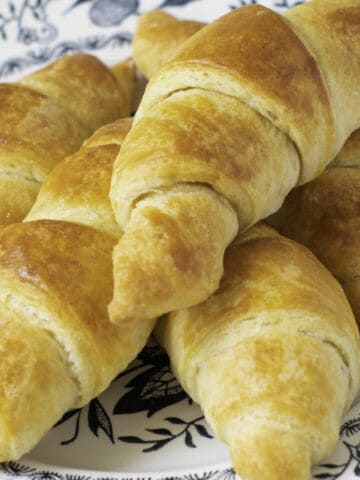 A plate with several golden-brown croissants stacked on top of each other, showing their flaky, layered texture-just like those made from an Easy Croissants recipe.