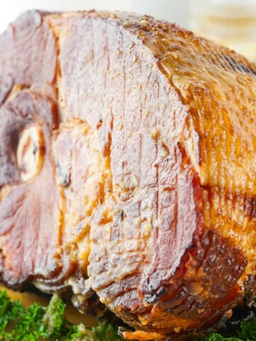 A close-up of a cooked, glazed spiral ham with a browned crust, resting on a bed of fresh green parsley—perfect for any spiral glazed ham recipe.