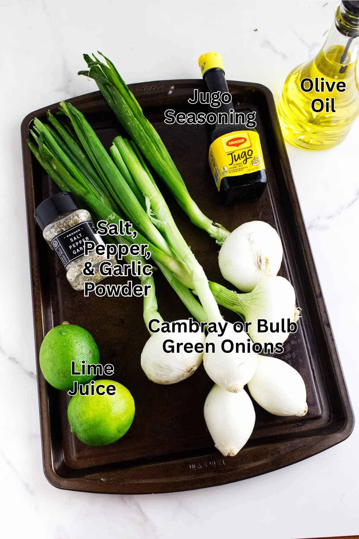 A baking sheet holds cambray or bulb green onions for Cebollitas Asadas (Mexican grilled onions), two limes, green onions, a bottle of olive oil, Jugo seasoning, and a container of salt, pepper, and garlic powder. Labels identify each ingredient.