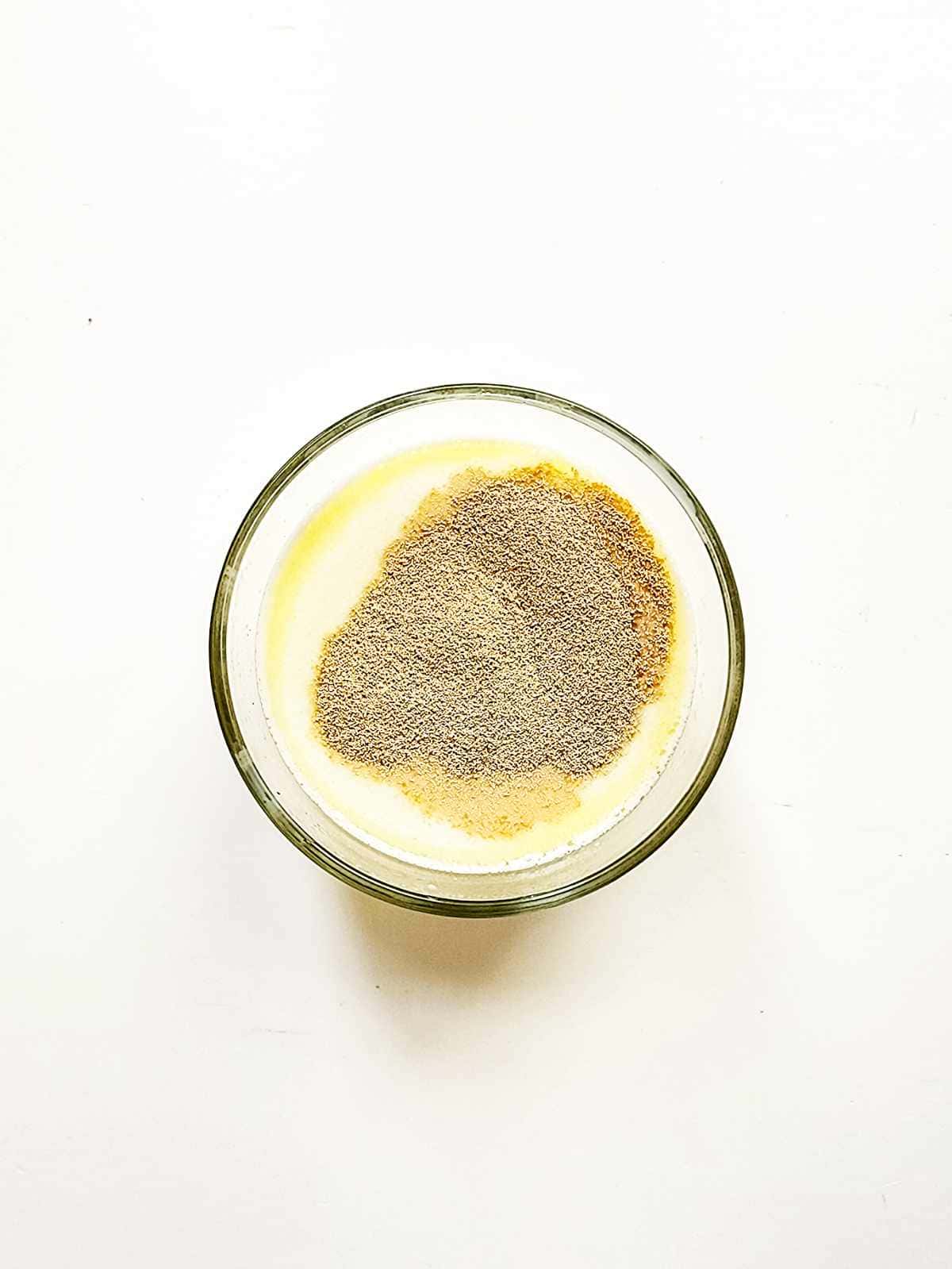 A glass bowl filled with a creamy yellow mixture topped with a generous layer of ground black pepper, reminiscent of the rich flavors found in New Orleans beignets, set against a plain white background.
