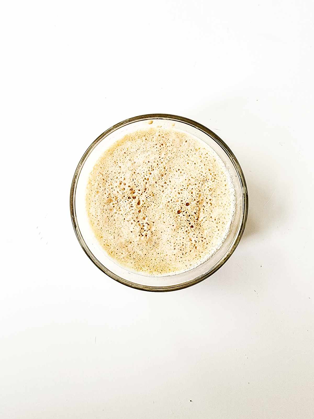 A clear glass filled with creamy, frothy coffee sits on a white background, viewed from above-perfectly paired with New Orleans beignets for an irresistible treat.
