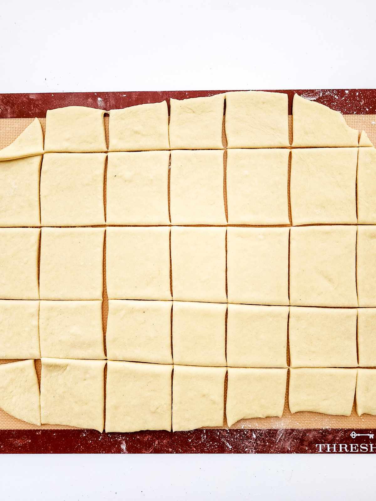 Rectangular dough rolled out on a floured surface and cut into even squares, just like classic New Orleans beignets, ready for baking or cooking.