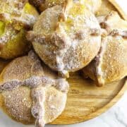 Round loaves of pan de muerto, traditional Day of the Dead bread, are topped with bone-shaped dough decorations and dusted with sugar, arranged on a wooden platter.