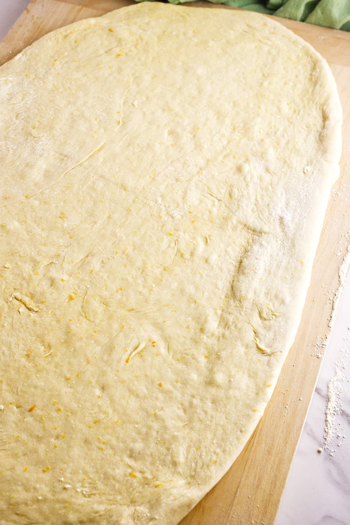Rosca de Reyes dough rolled into a rectangle on a floured wooden board.