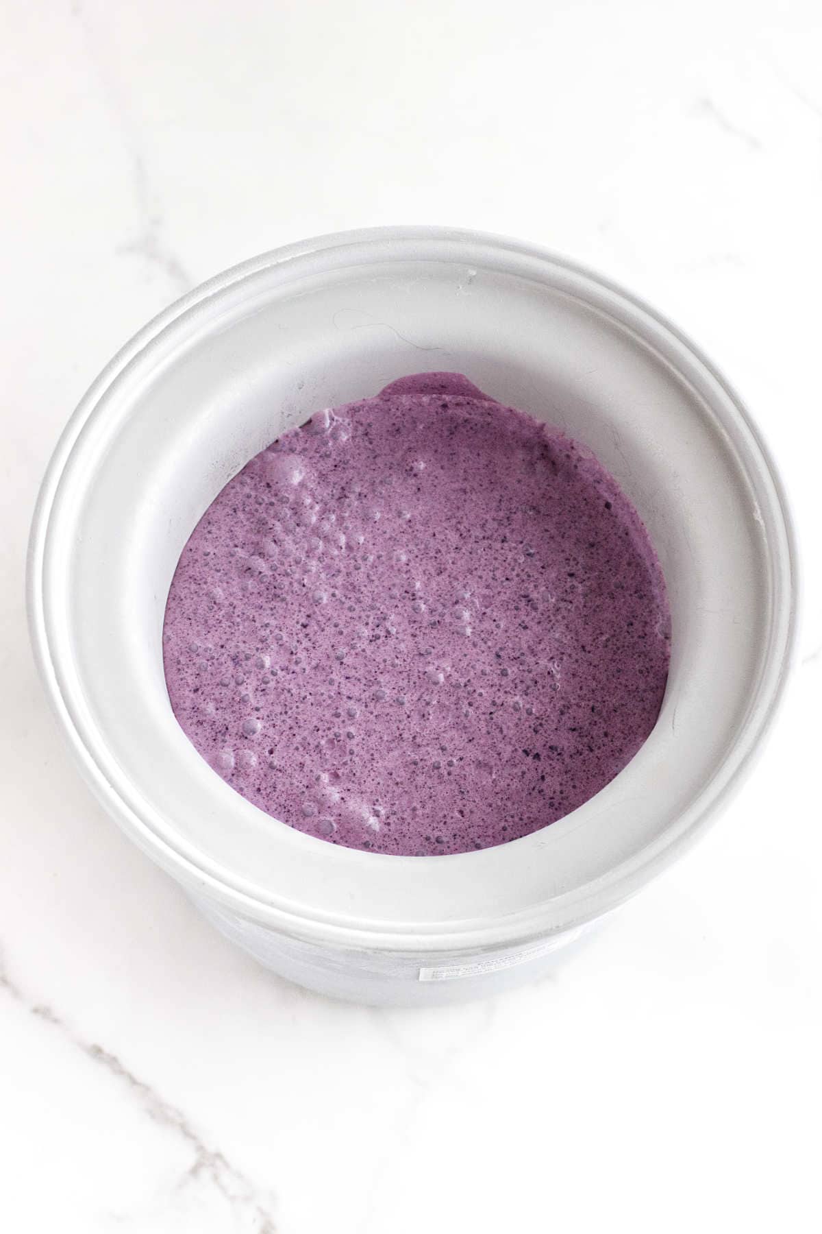 A metal mixing bowl filled with smooth, thick acai berry ice cream mixture sits on a white marble surface.