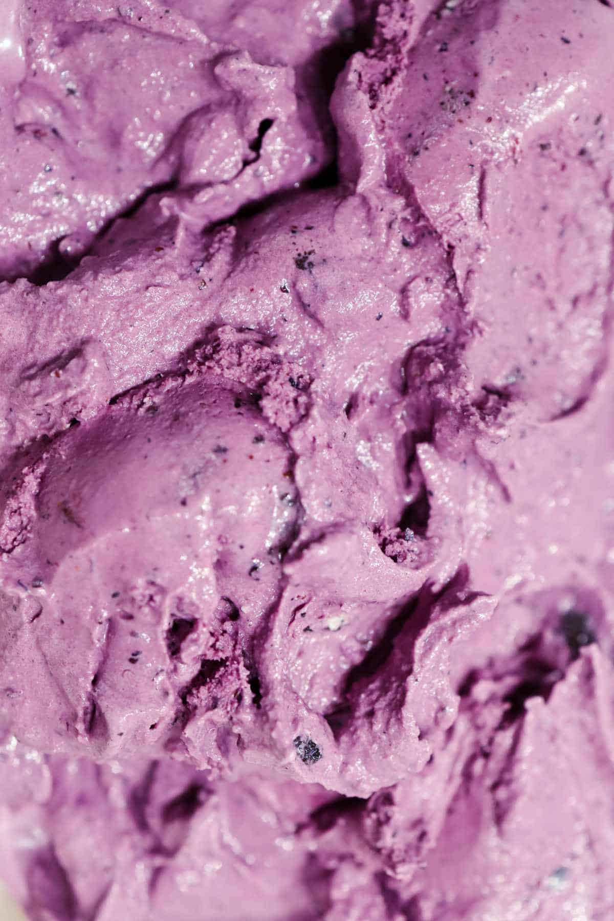 Close-up of creamy, textured acai berry ice cream with specks of darker color, suggesting the presence of real berry pieces or flavoring.