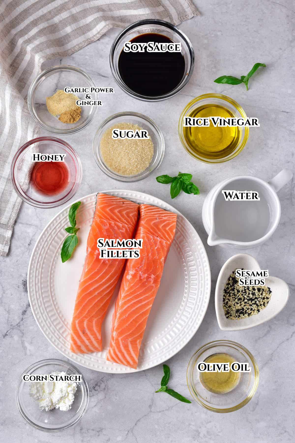 Ingredients for a salmon recipe arranged on a marble surface: raw salmon fillets on a plate, and small bowls containing soy sauce, rice vinegar, olive oil, water, sesame seeds, sugar, honey, garlic powder, ginger, and corn starch.