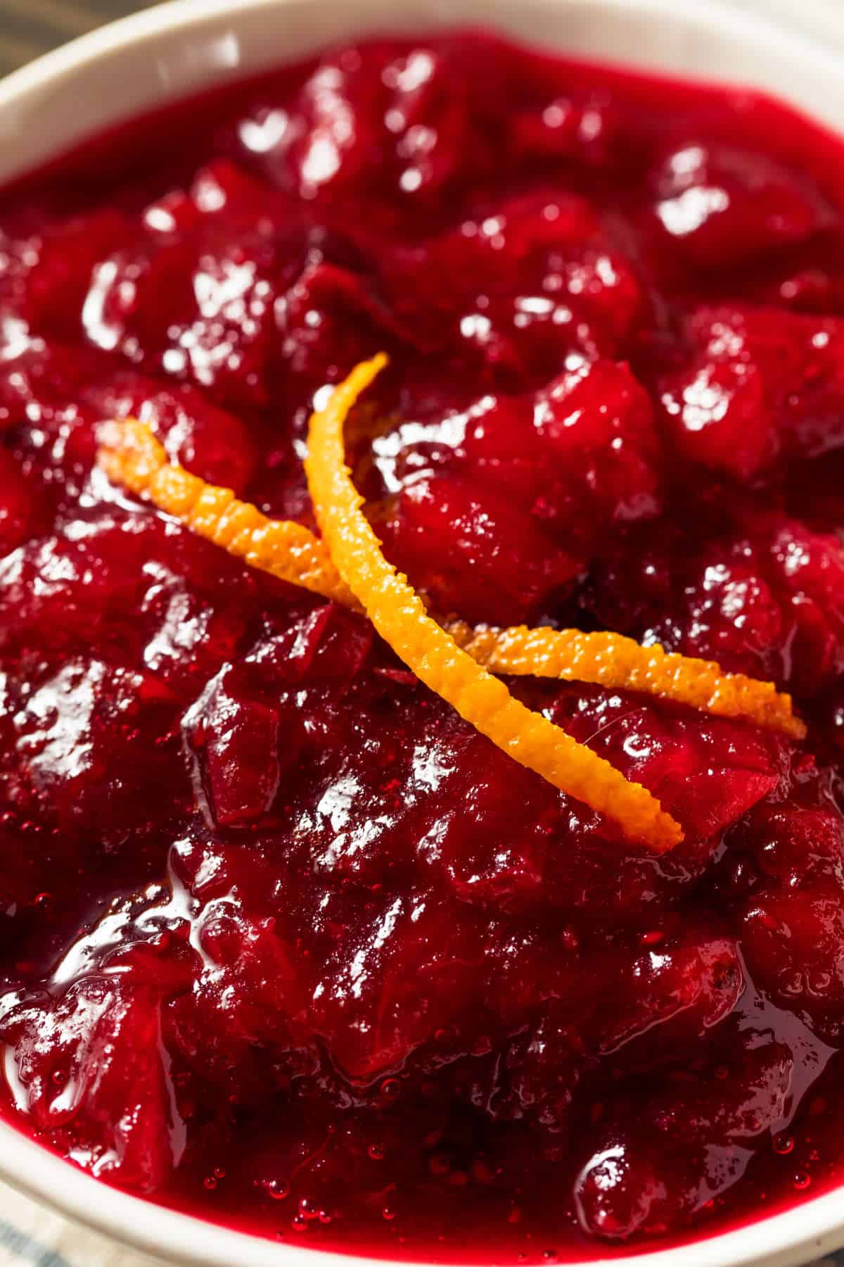 A close-up of a bowl filled with chunky homemade cranberry orange sauce, garnished with thin orange zest strips on top.
