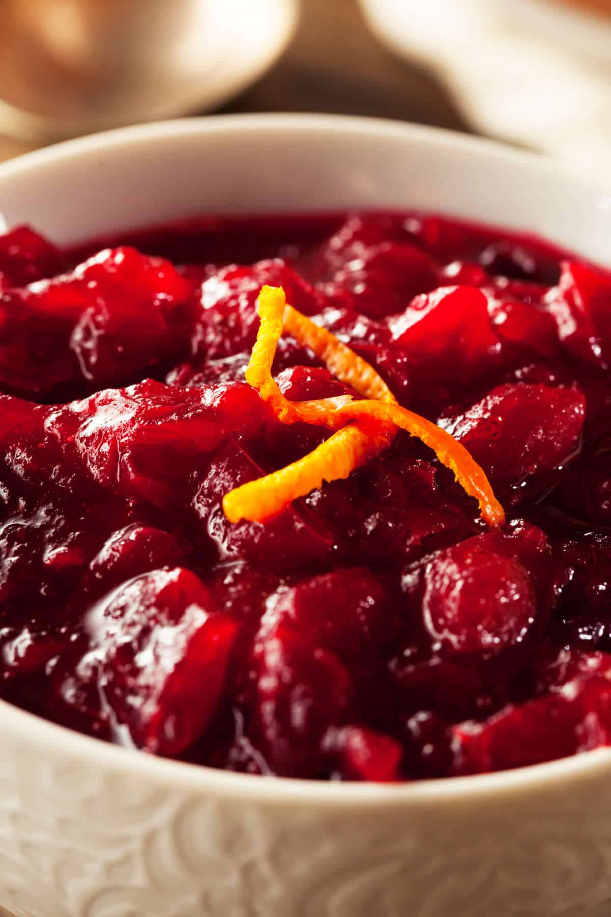 A close-up of a bowl filled with chunky homemade cranberry orange sauce, garnished with thin strips of orange zest.