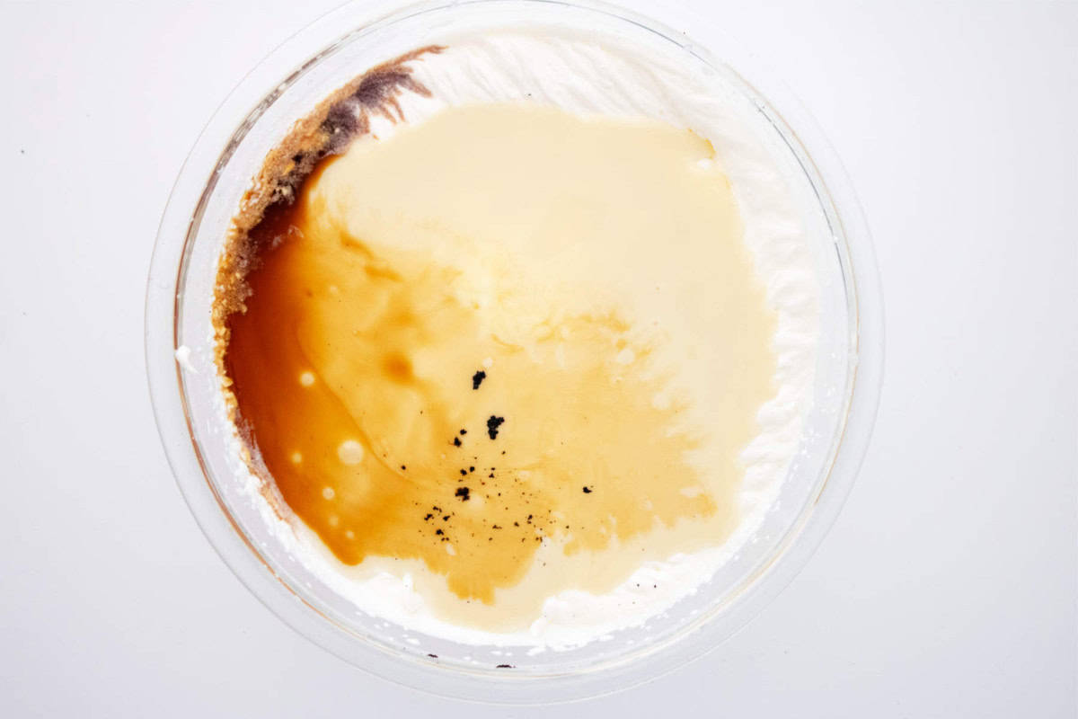 A glass bowl seen from above contains separated layers of heavy cream, sweetened condensed milk, vanilla extract, and vanilla bean specks—ingredients ready to be mixed for homemade ice cream maker vanilla ice cream.