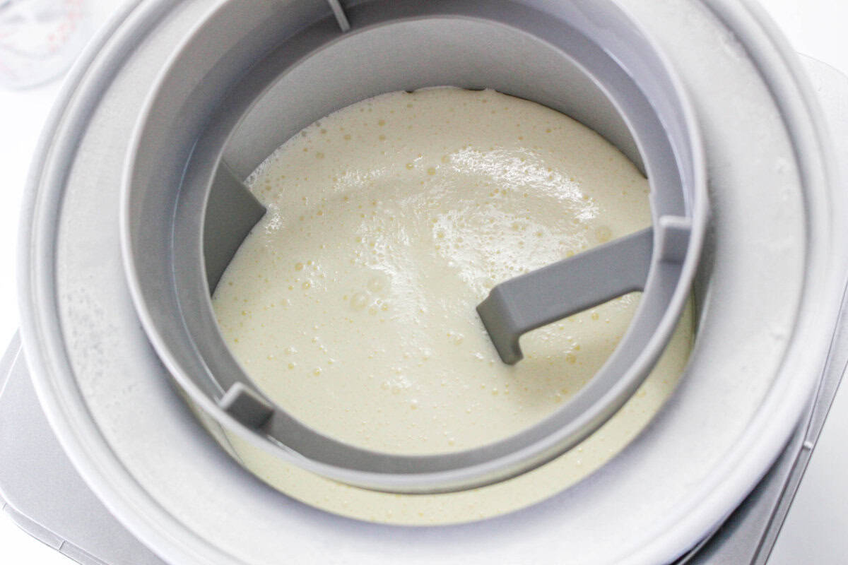 Close-up of vanilla ice cream mixture being churned in an ice cream maker, showing the creamy liquid slowly thickening around the mixer blade as homemade vanilla ice cream begins to form.