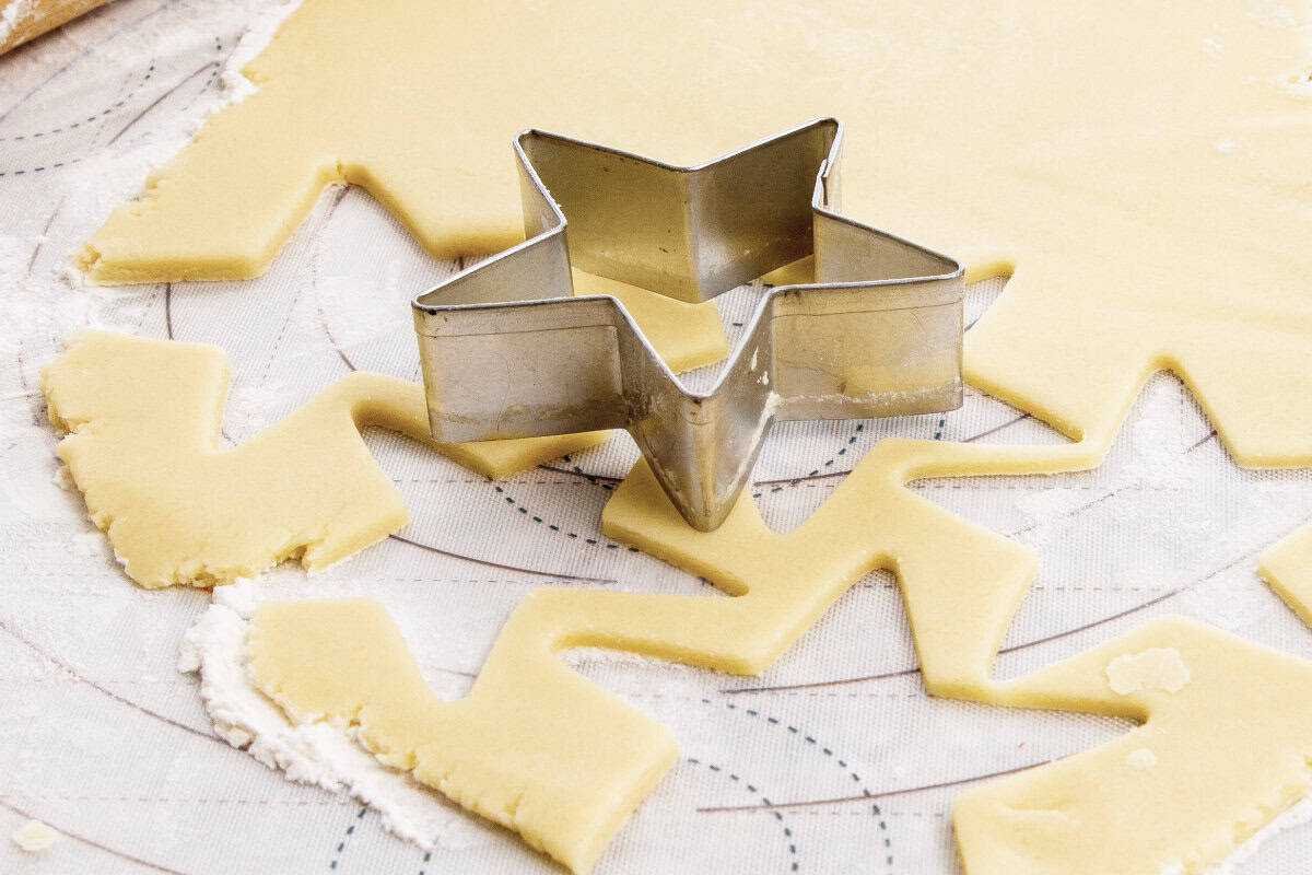 A metal star-shaped cookie cutter sits on rolled-out dough with star shapes cut out, ready for baking-a perfect start for a festive mixed berry sheet pan pie. Traces of flour and a patterned surface are visible beneath the dough.