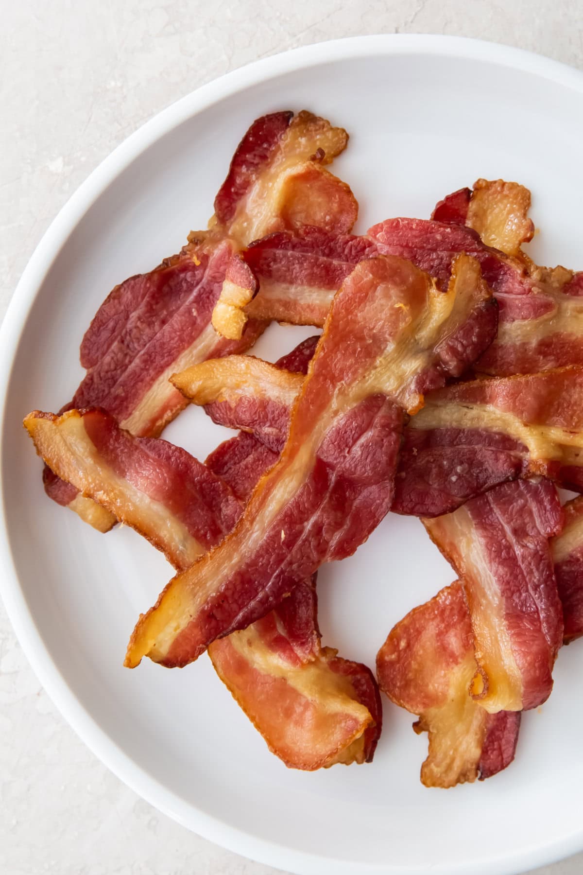Crispy air fryer bacon strips arranged on a white plate, viewed from above on a light-colored surface.