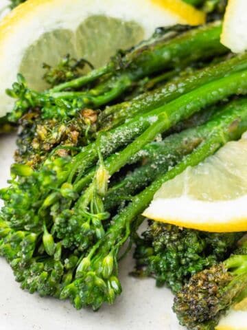 Close-up of air fried broccolini garnished with coarse salt and served with fresh lemon slices on a white plate.