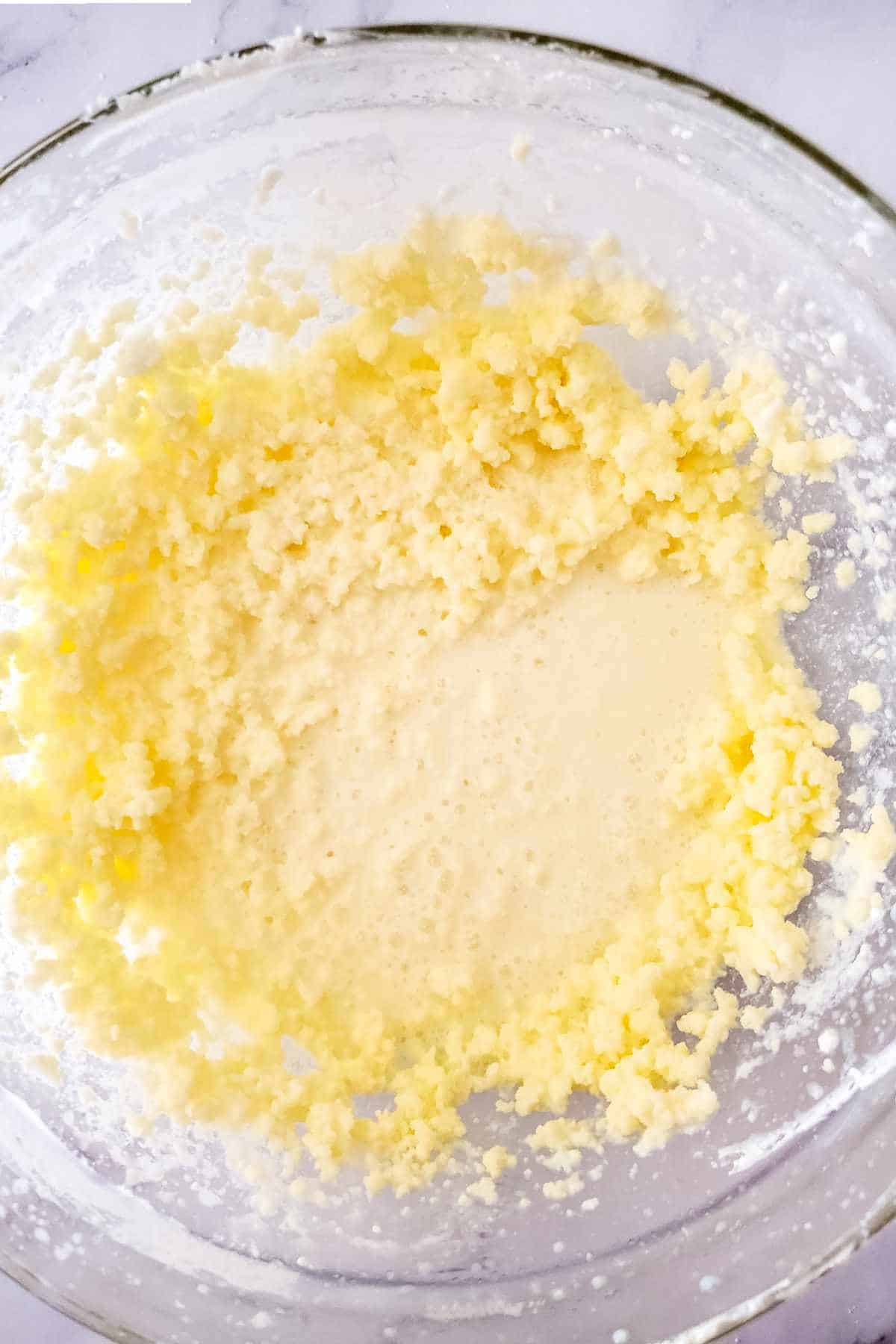 Butter beginning to separate from buttermilk in a glass bowl.