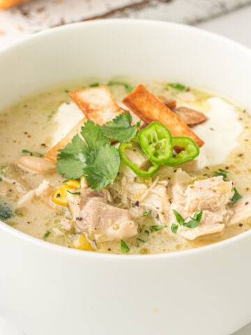 A bowl of creamy easy slow cooker white chicken chili garnished with fresh cilantro, sliced green chili, crispy tortilla strips, and a dollop of sour cream.