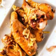 A close-up of crispy garlic parmesan chicken wings on a white plate, topped with shredded cheese and seasonings.