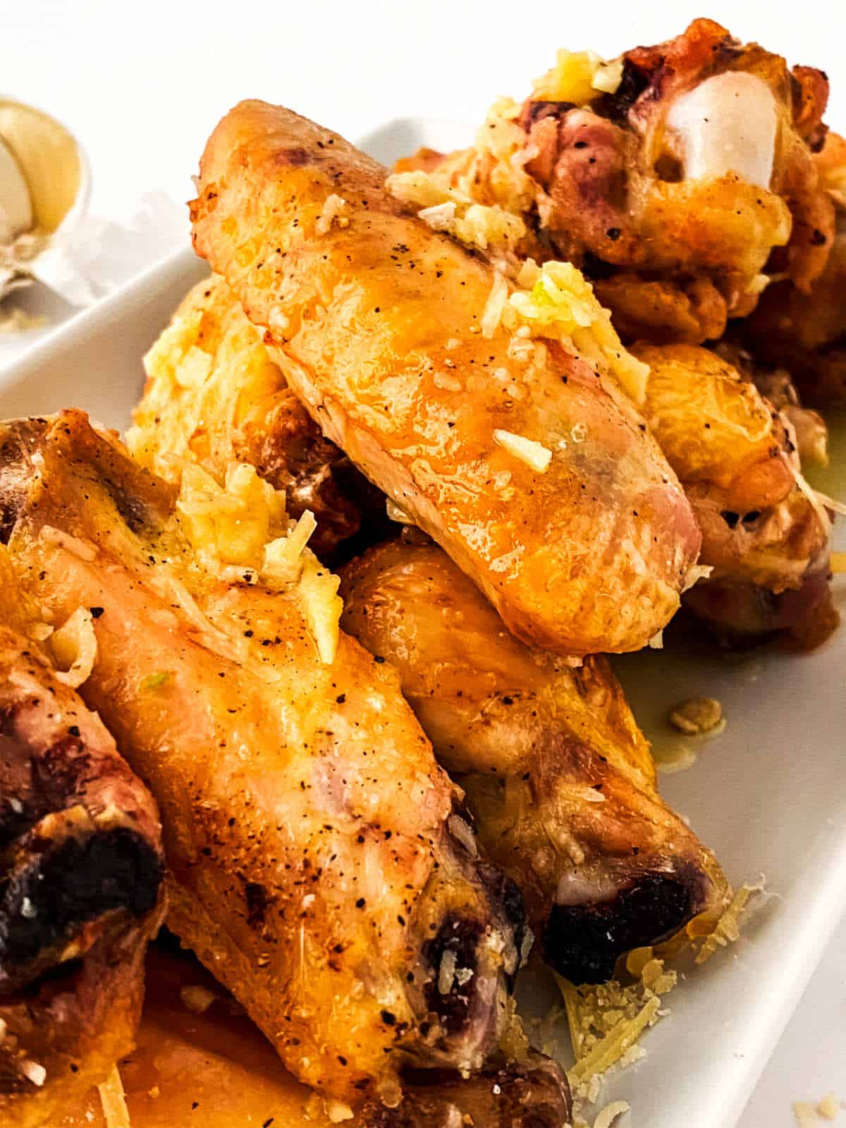 A close-up of golden-brown garlic parmesan chicken wings on a white plate, topped with grated cheese and seasonings.
