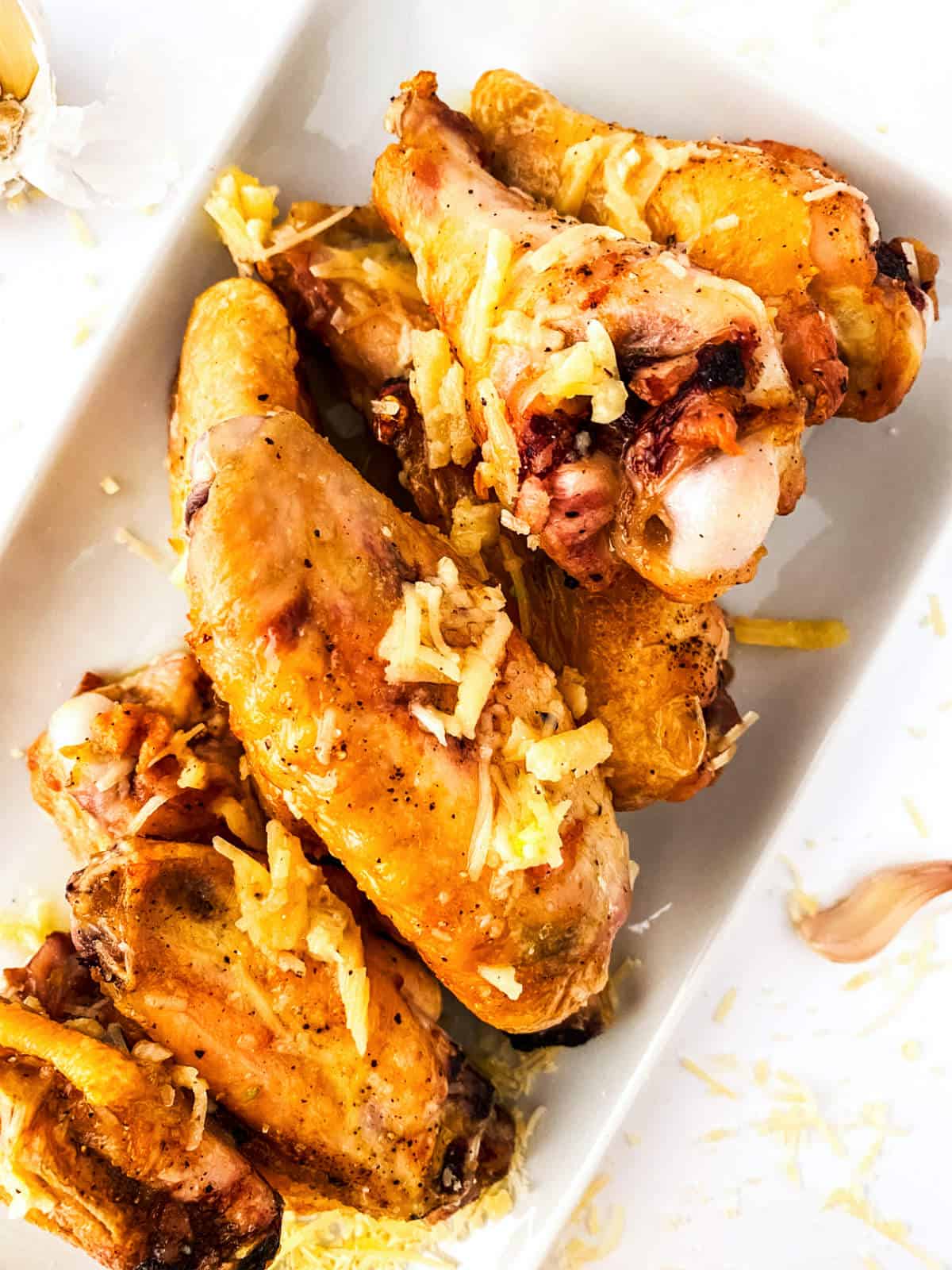 A plate of golden-brown garlic parmesan chicken wings, topped with shredded cheese and served on a white rectangular dish.