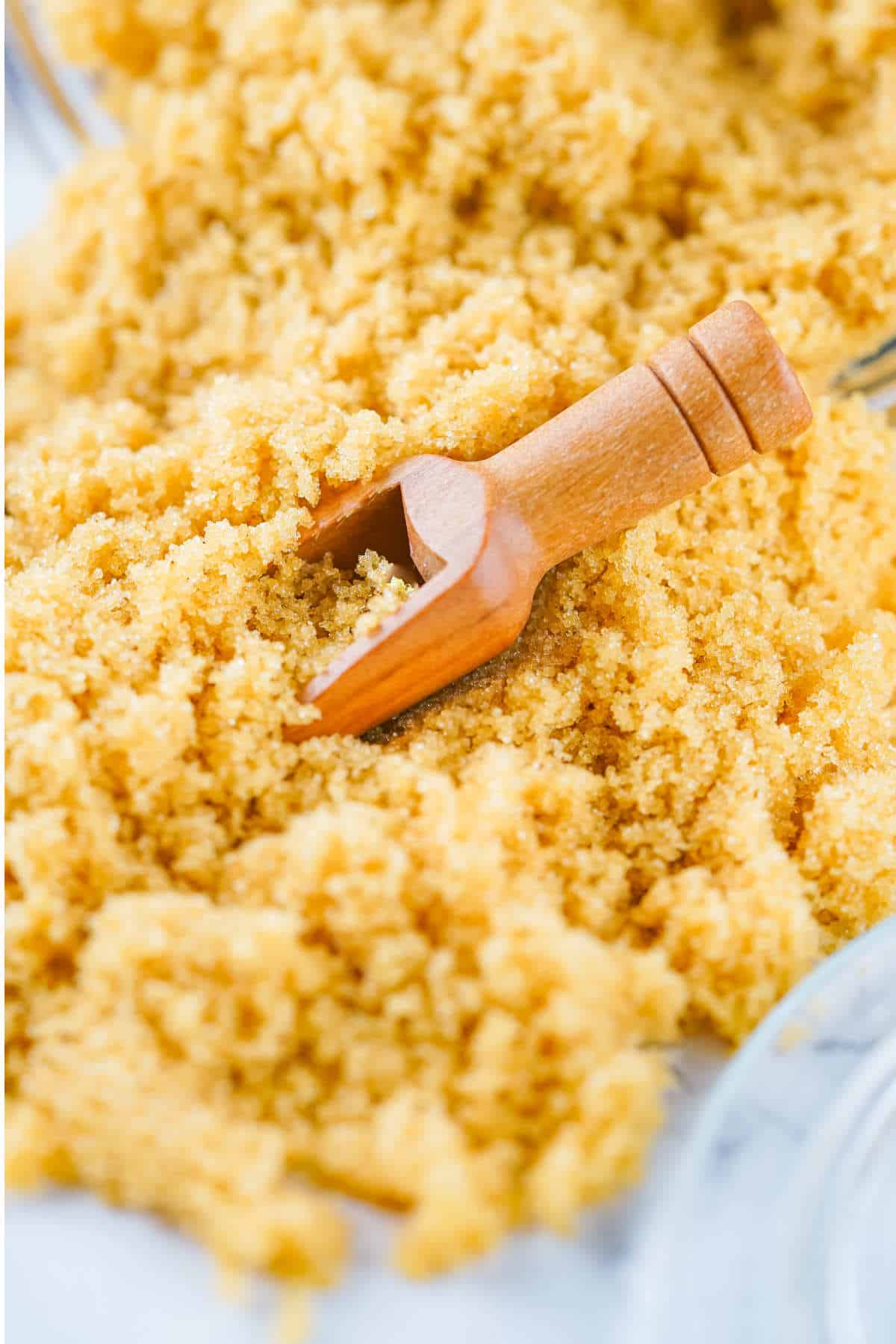 A small wooden scoop rests in a pile of homemade brown sugar substitute, with granules scattered around.