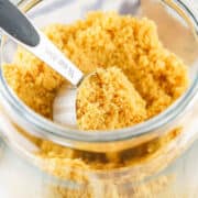 A metal ¼ cup measuring scoop filled with homemade brown sugar sits inside a glass jar also filled with brown sugar.