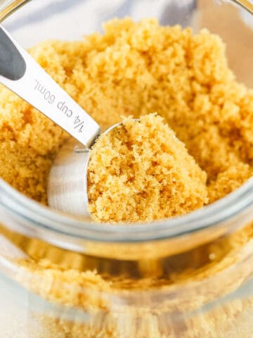 A metal ¼ cup measuring scoop filled with homemade brown sugar sits inside a glass jar also filled with brown sugar.