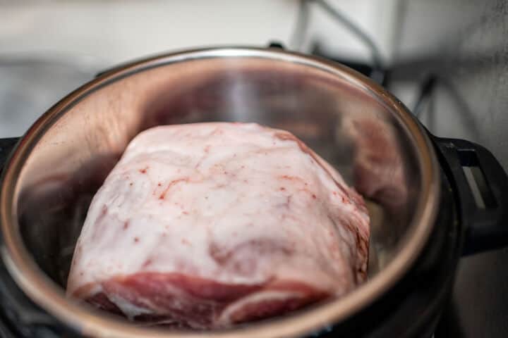 Seasoned pork butt searing in the stainless steel insert of an Instant Pot.