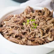 Tender Instant Pot pork butt shredded in a white serving dish with tongs nearby.