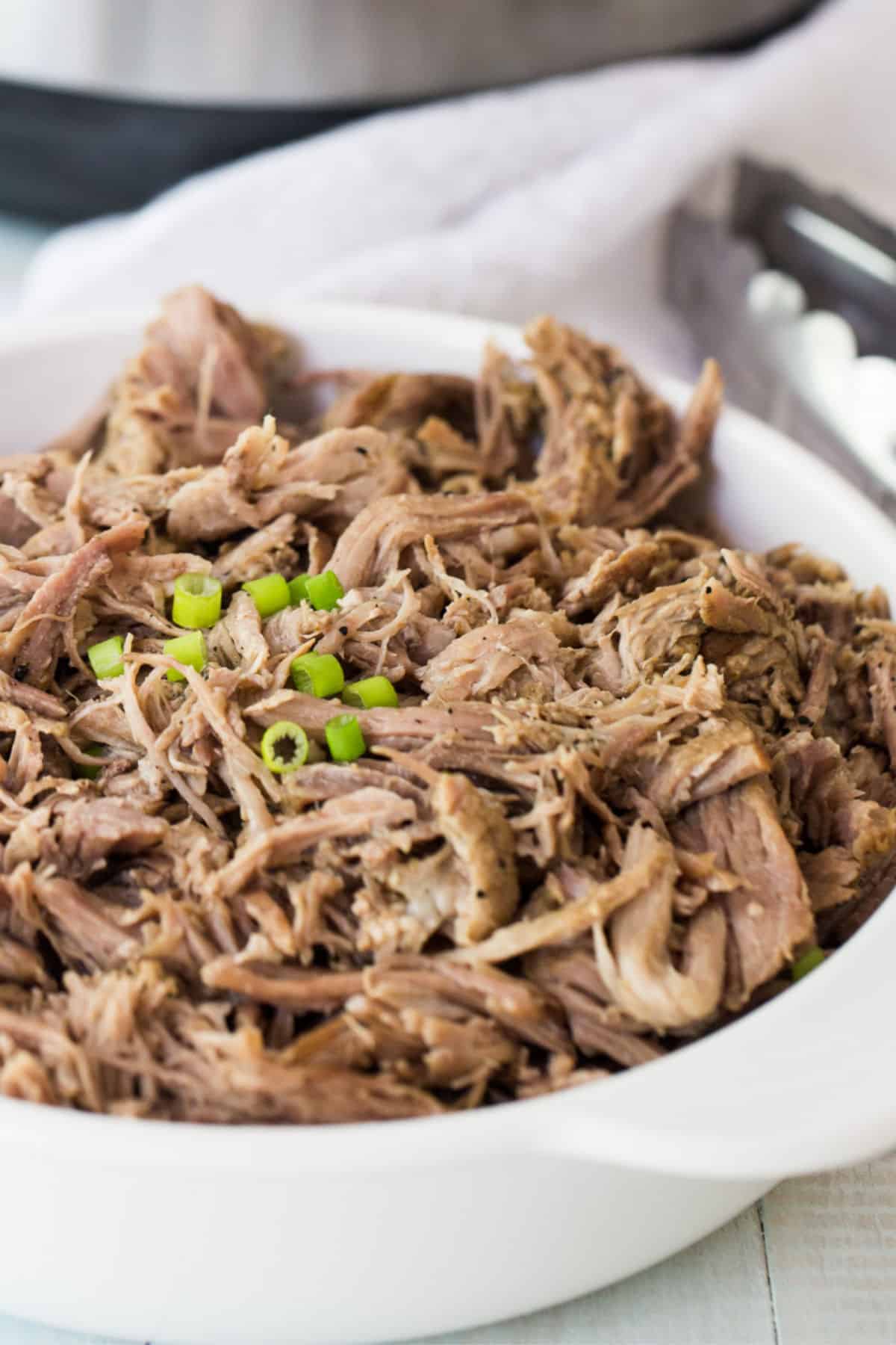 Tender Instant Pot pork butt shredded in a white serving dish with tongs nearby.