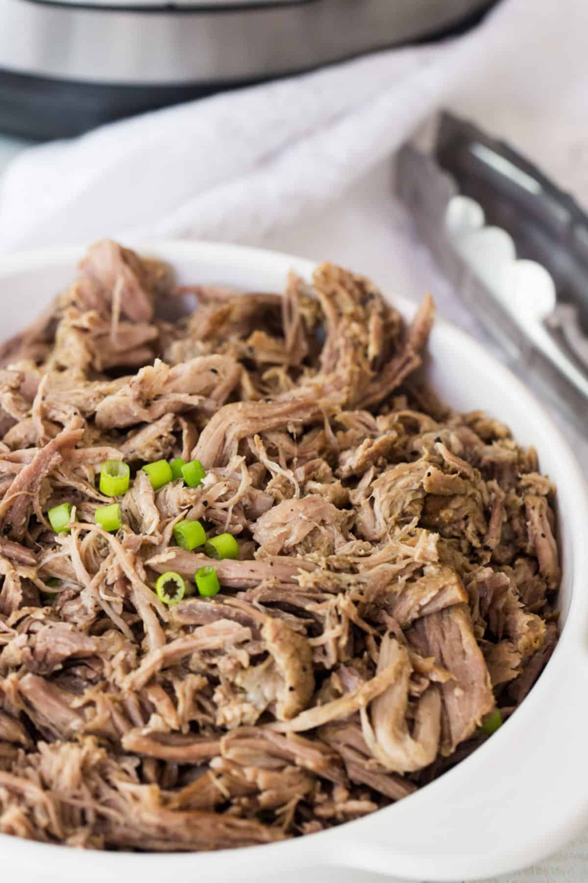 Shredded Instant Pot pork butt served in a white bowl with sliced green onions.