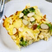 A close-up of a Low Carb Chicken and Swiss casserole with broccoli, topped with sliced almonds and melted cheese, served on a white plate.