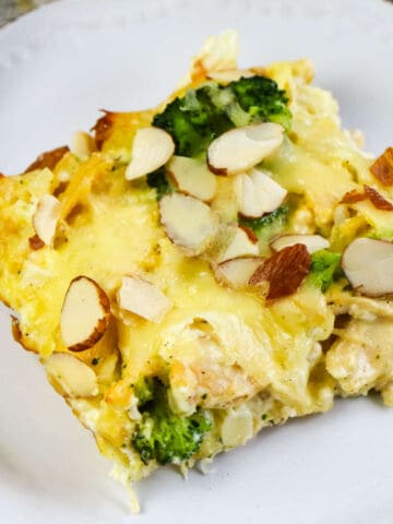 A close-up of a Low Carb Chicken and Swiss casserole with broccoli, topped with sliced almonds and melted cheese, served on a white plate.