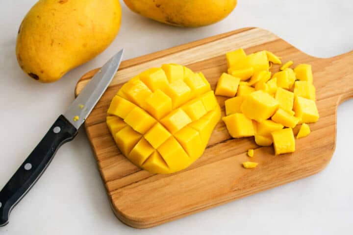 A mango on a cutting board next to a knife, ready to be sliced for a refreshing mangonada.