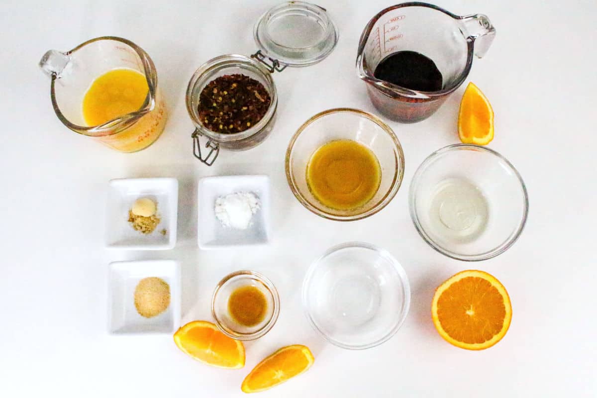 Measured ingredients for orange teriyaki sauce including orange juice, soy sauce, spices, and vinegar on a white surface.
