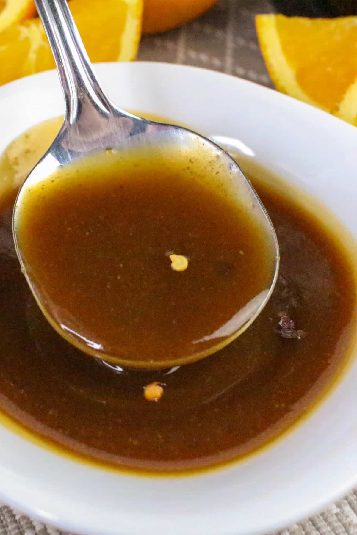 Spoon lifting thick orange teriyaki sauce from a white bowl.