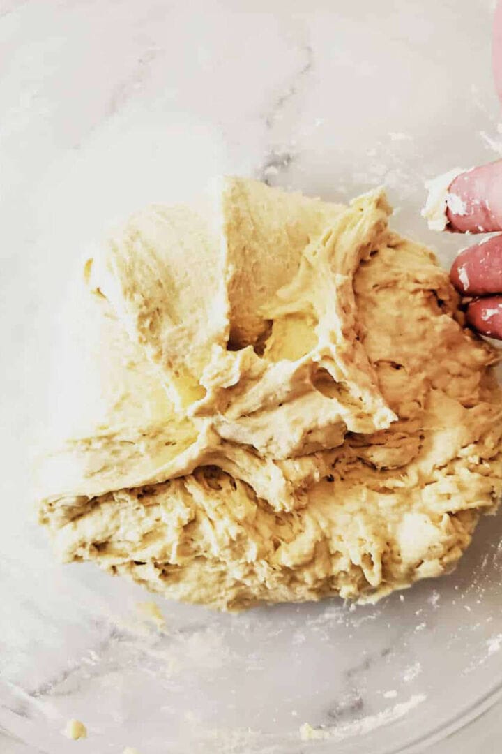 A close-up of a hand mixing sticky, pale yellow dough for Moroccan semolina bread on a lightly floured surface, with the dough showing a rough texture.