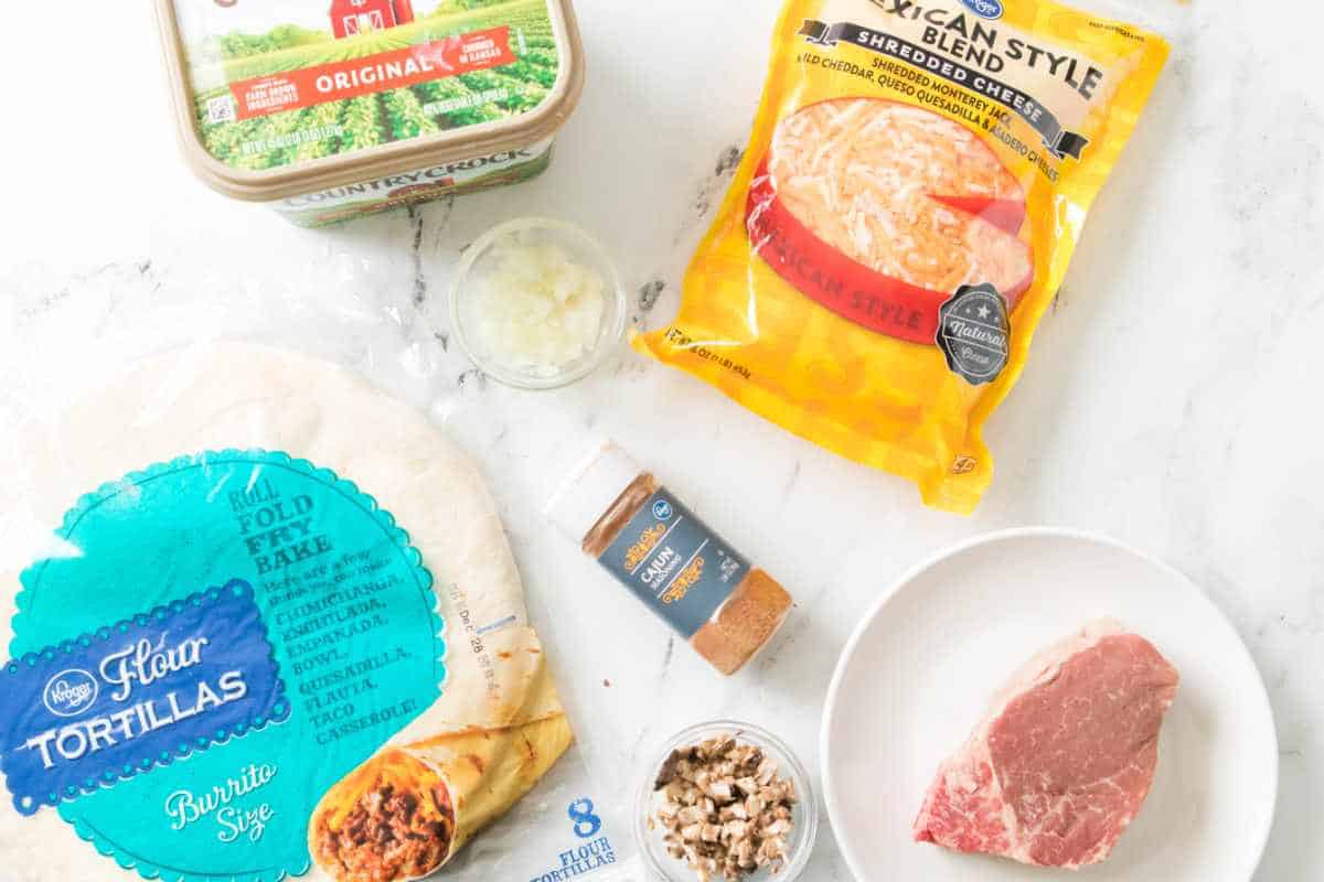 Ingredients for steak quesadillas with flour tortillas, steak, shredded cheese, onions, mushrooms, and seasoning.
