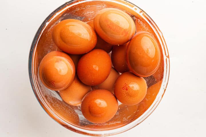 A glass bowl filled with brown eggs submerged in water, viewed from above on a white background-perfect for preparing devuled eggs.
