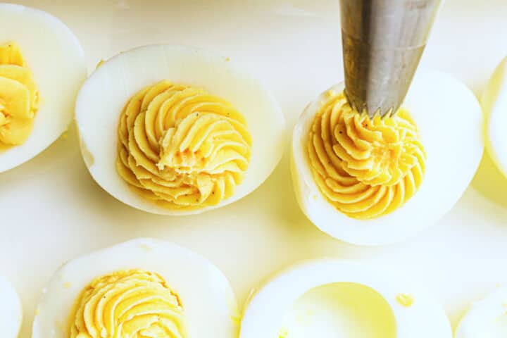 A close-up of devuled eggs being filled with a creamy yolk mixture using a piping bag with a star tip, creating a decorative swirl inside the egg whites.