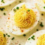 A close-up of devuled eggs, halved and filled with a creamy, piped yolk mixture, garnished with chopped chives and a sprinkle of paprika and black pepper.