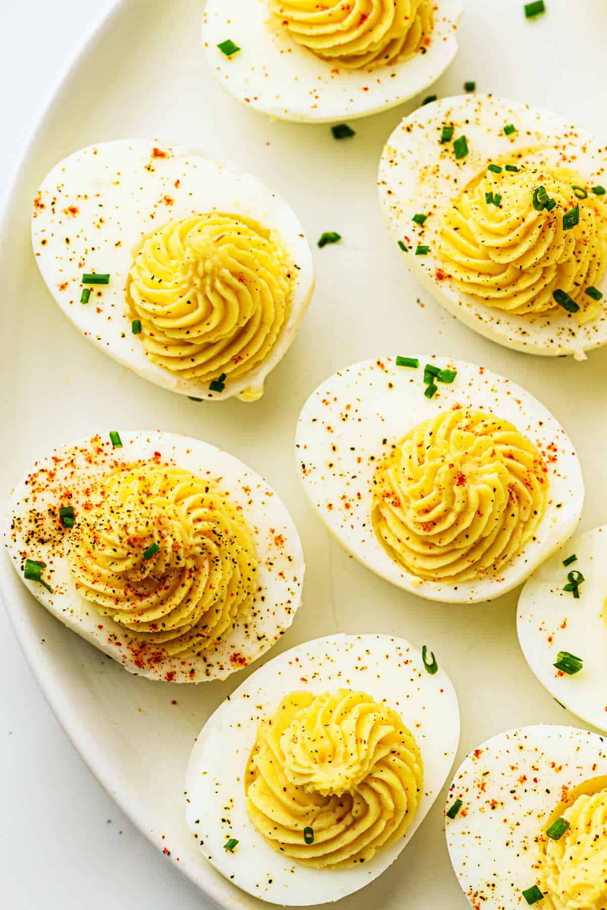 A close-up of devuled eggs on a white plate, garnished with chopped chives and a sprinkle of paprika on the creamy yellow yolk filling.