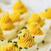 A close-up of devuled eggs topped with creamy yellow filling and sprinkled with chopped chives, arranged neatly on a white platter.