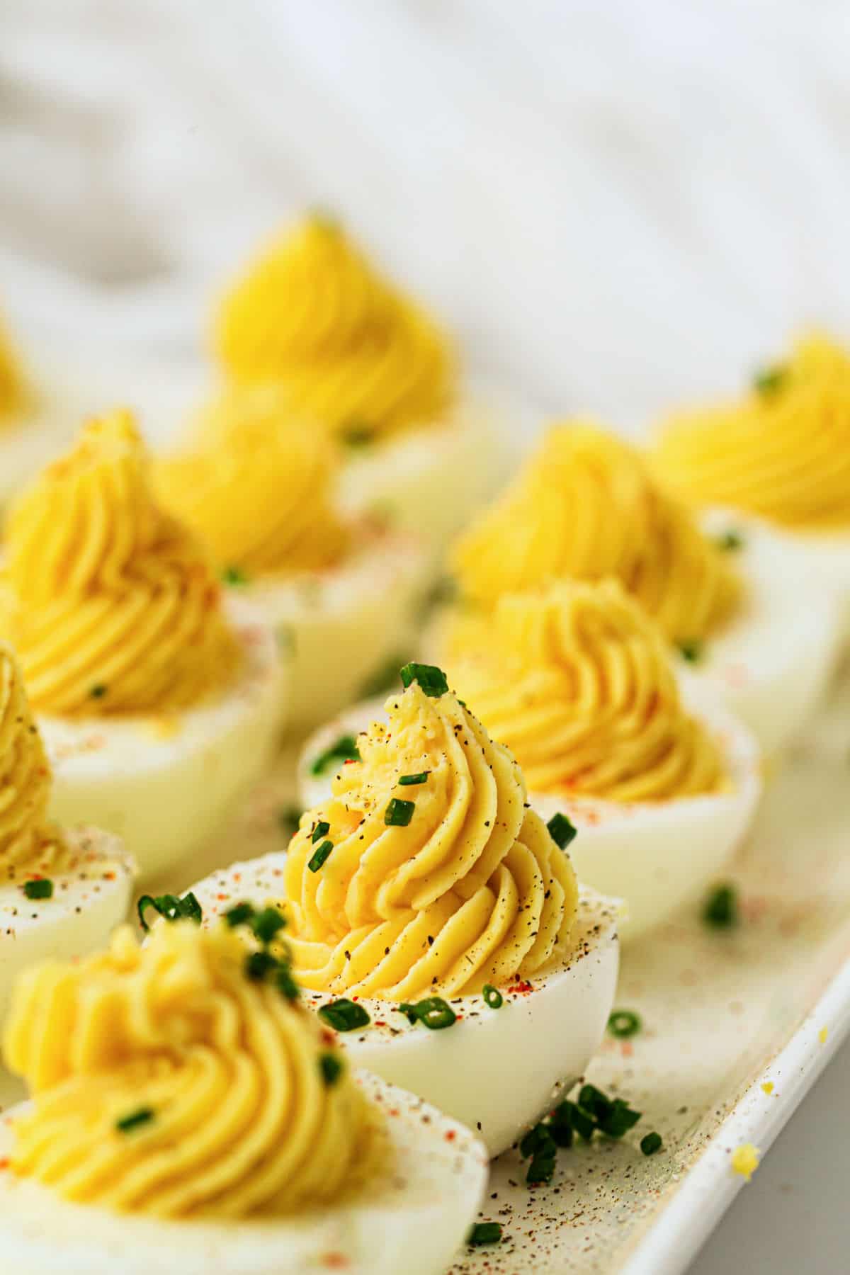 A close-up of devuled eggs topped with creamy yellow filling and sprinkled with chopped chives, arranged neatly on a white platter.