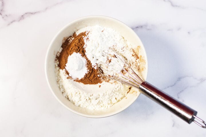 A white bowl on a marble surface holds flour, cinnamon, baking powder, and cornstarch being whisked together-the perfect start for delicious red velvet chocolate chip cookies.