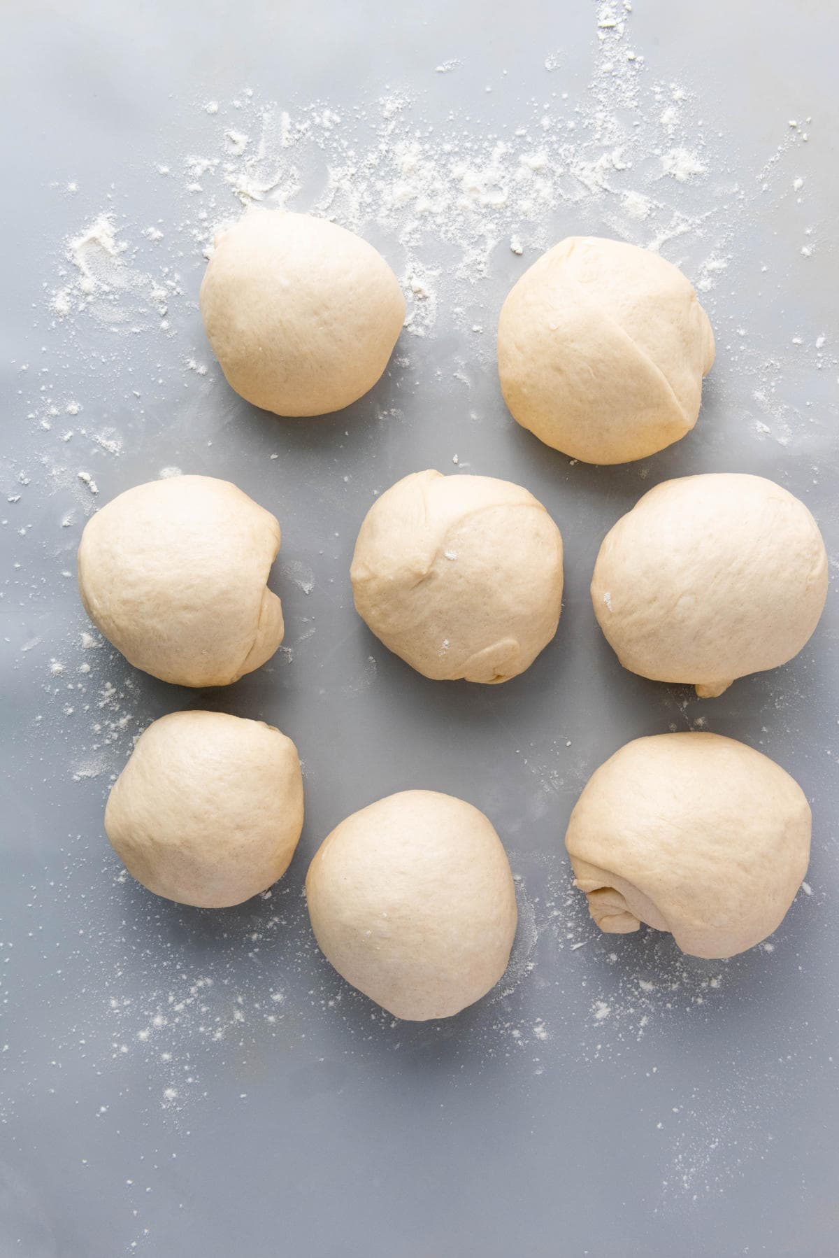 Eight round balls of dough are arranged on a lightly floured surface, ready for baking or cooking.