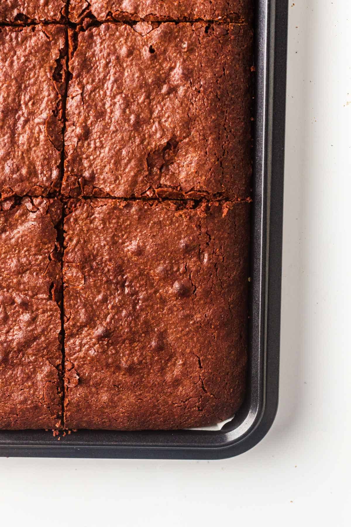 Sheet pan brownies cut into squares in a half sheet pan with a shiny crackled top.