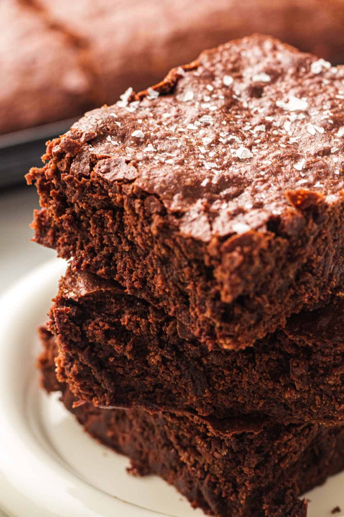 Stacked sheet pan brownies with a fudgy center and crackled top on a plate.