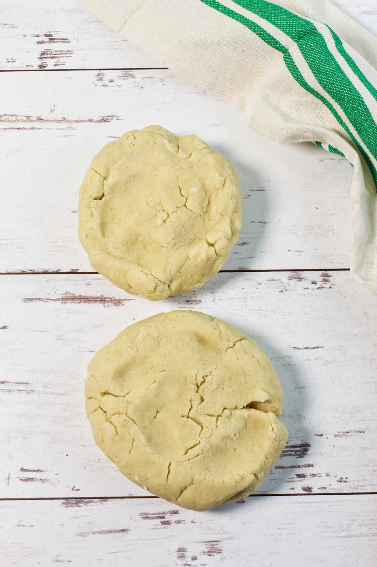 Two round stamped shortbread cookies rest on a white wooden surface, with a cream and green striped cloth partially visible in the upper right corner.