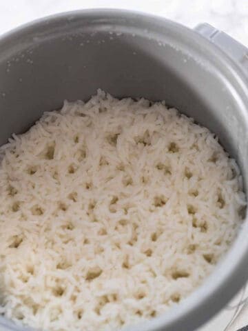 A close-up view of cooked white rice inside a gray rice cooker, with the rice evenly spread out across the bottom of the pot.