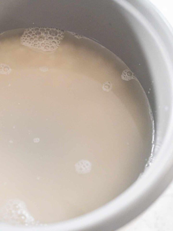 A close-up of cloudy water with bubbles on the surface inside a rice cooker pan.